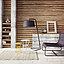 Wohnraum mit Holzlamellenwand, Lounge‑Stuhl, Stehleuchte, kleinen Beistelltischen und Teppich