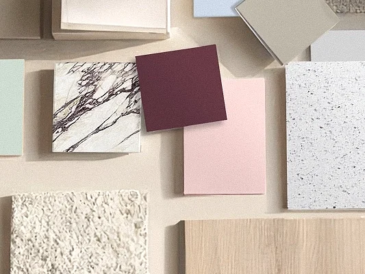 Hand legt Oberflächenmuster in Terrazzo-, Marmor- und Holzoptik sowie Unifarben zu einem Moodboard zusammen: Co-Creation für Dekoroberflächen