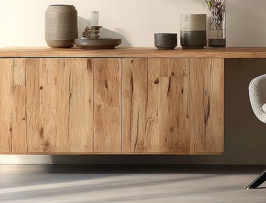 Schwebendes Sideboard aus hellem, naturbelassenem Holz mit sichtbarer Maserung vor einer hellen Wand, darauf Keramikvasen, eine Schale und eine Glasvase mit Grünpflanze. Rechts ein Sessel mit beige Bouclé-Bezug und schwarzem Sternfuß.